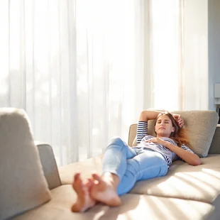 Lichtdurchlässig - Durch eine Gardine vor neugierigen Blicken geschützt, liegt eine Frau auf dem Sofa.