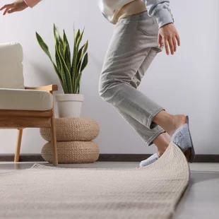 Illustration - Ihr Experte für schönes Wohnen - Frau stolpert zu Hause über Teppich, Nahaufnahme.